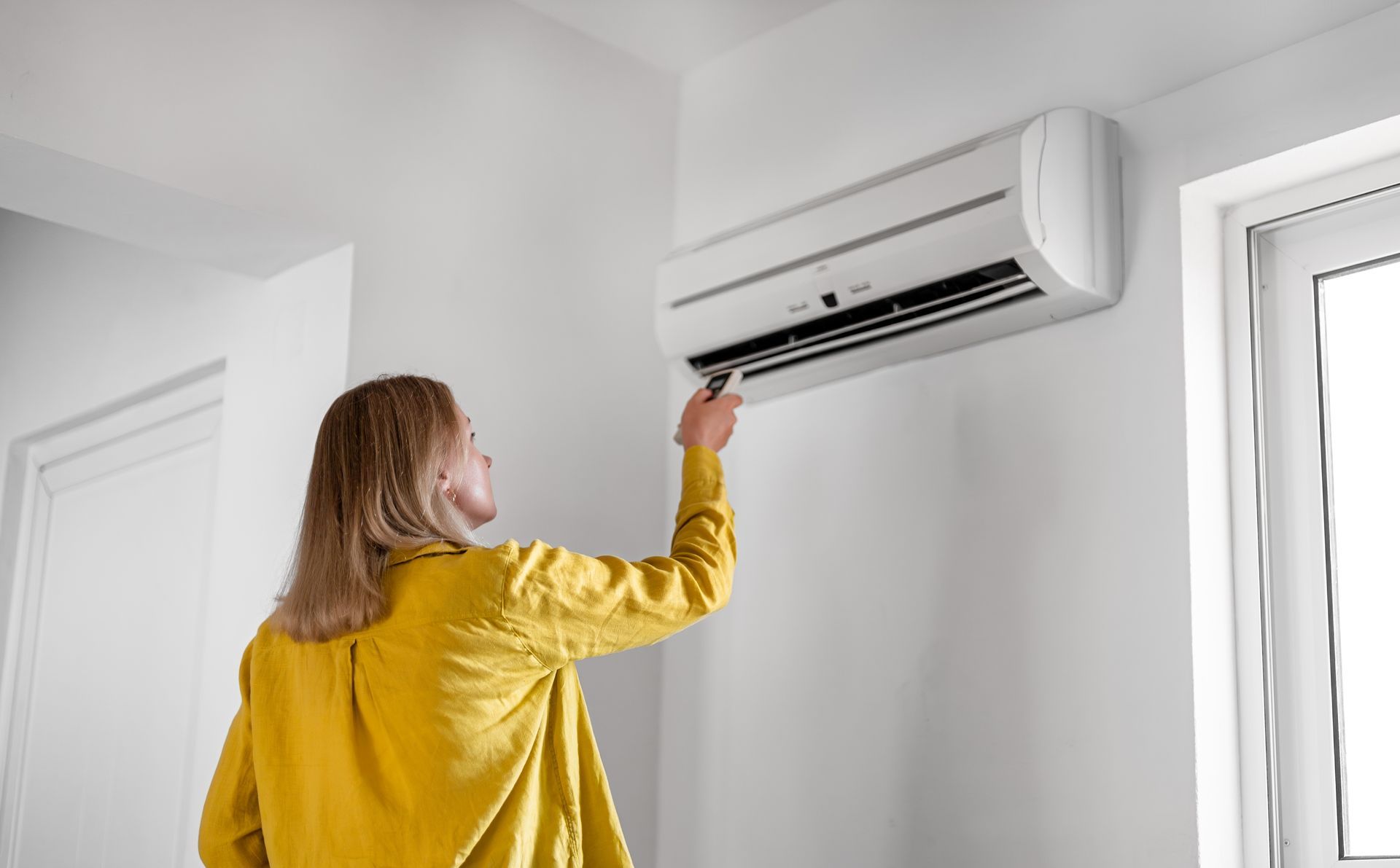 A woman in a yellow shirt is adjusting the air conditioner in a room.