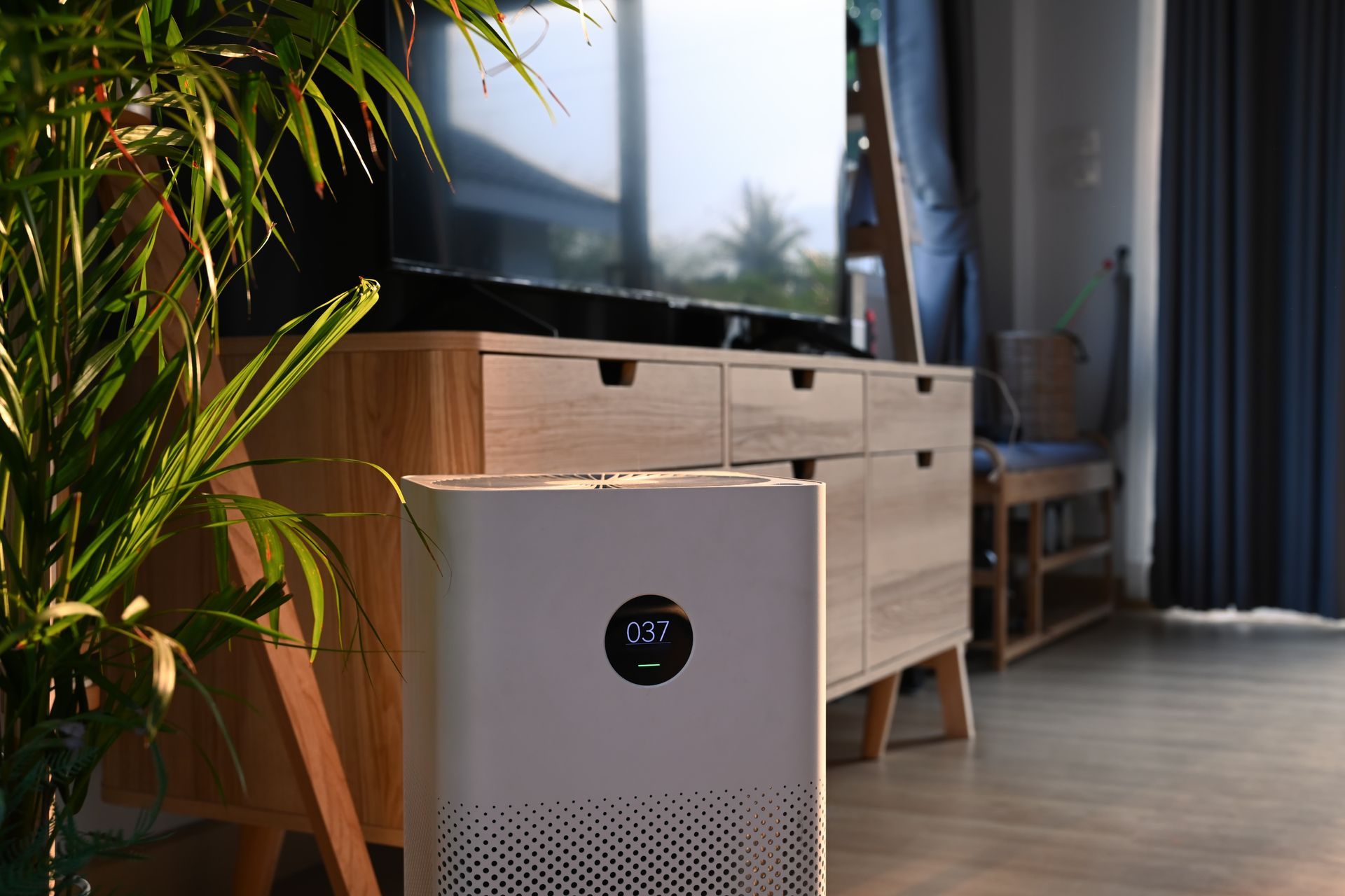 Air purifier in a sunlit living room with a TV and wooden console.
