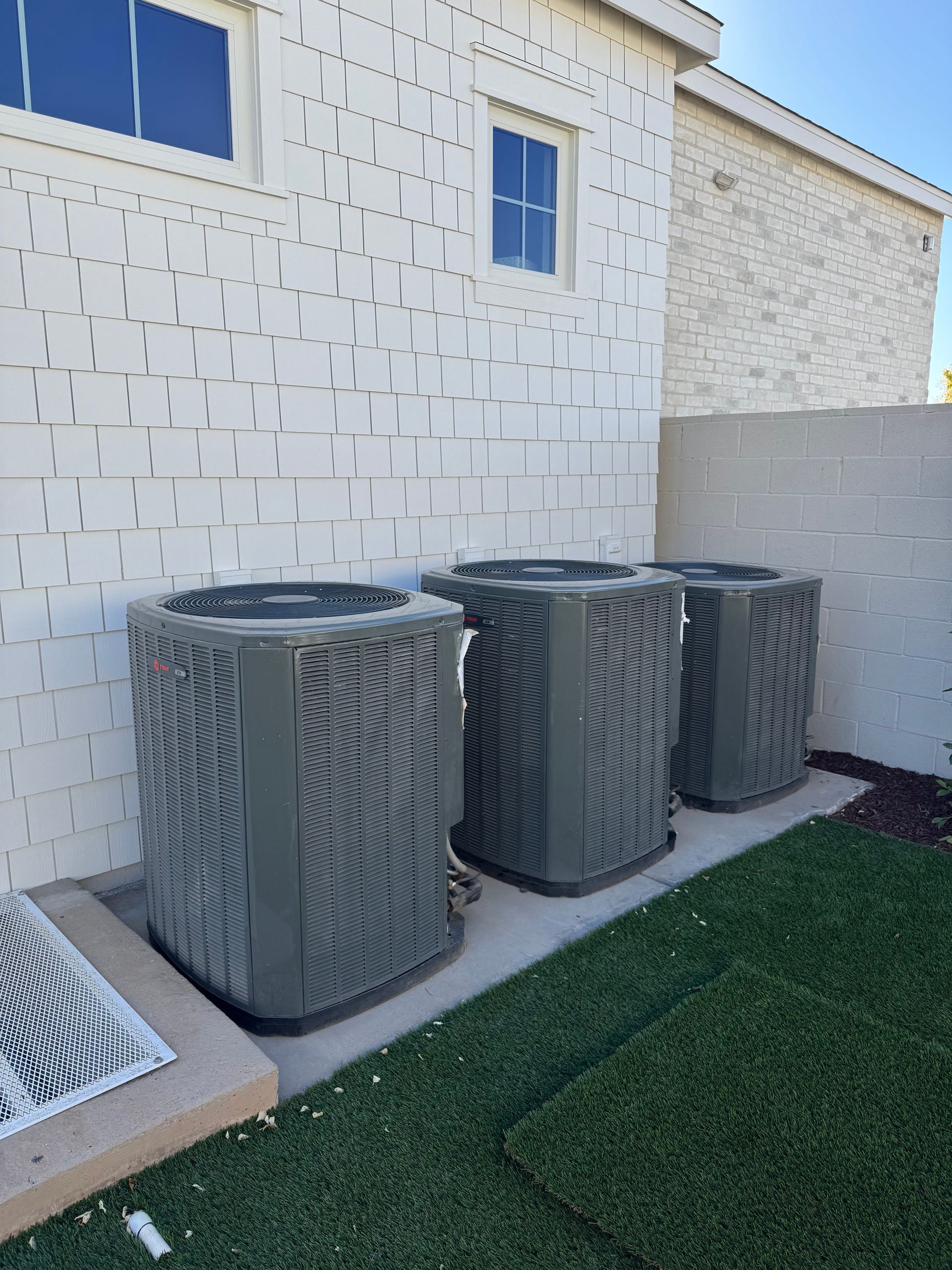 Three air conditioners are sitting in front of a white brick building.