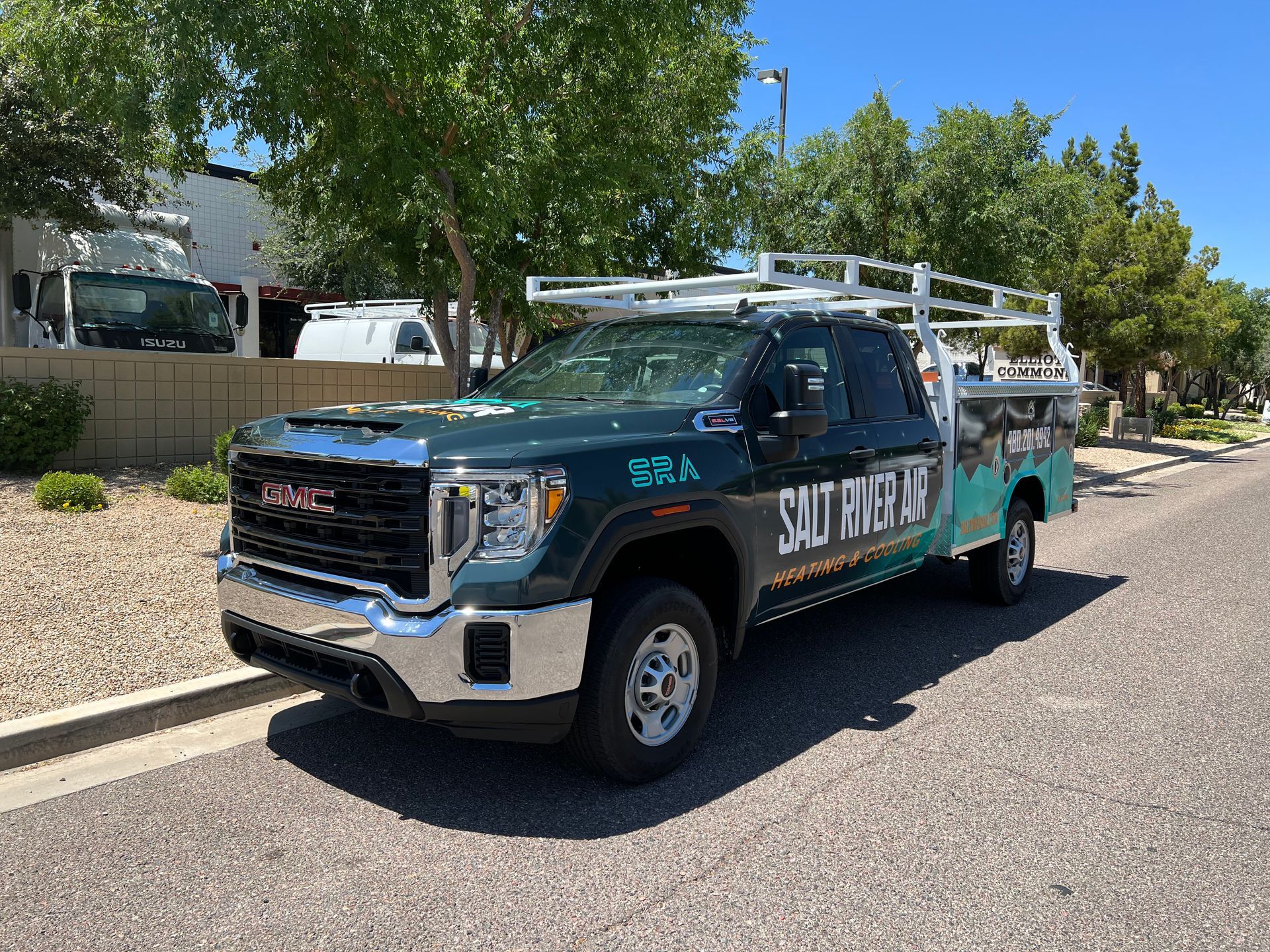 Green utility truck parked on a sunny street, with a ladder rack and large side lettering.