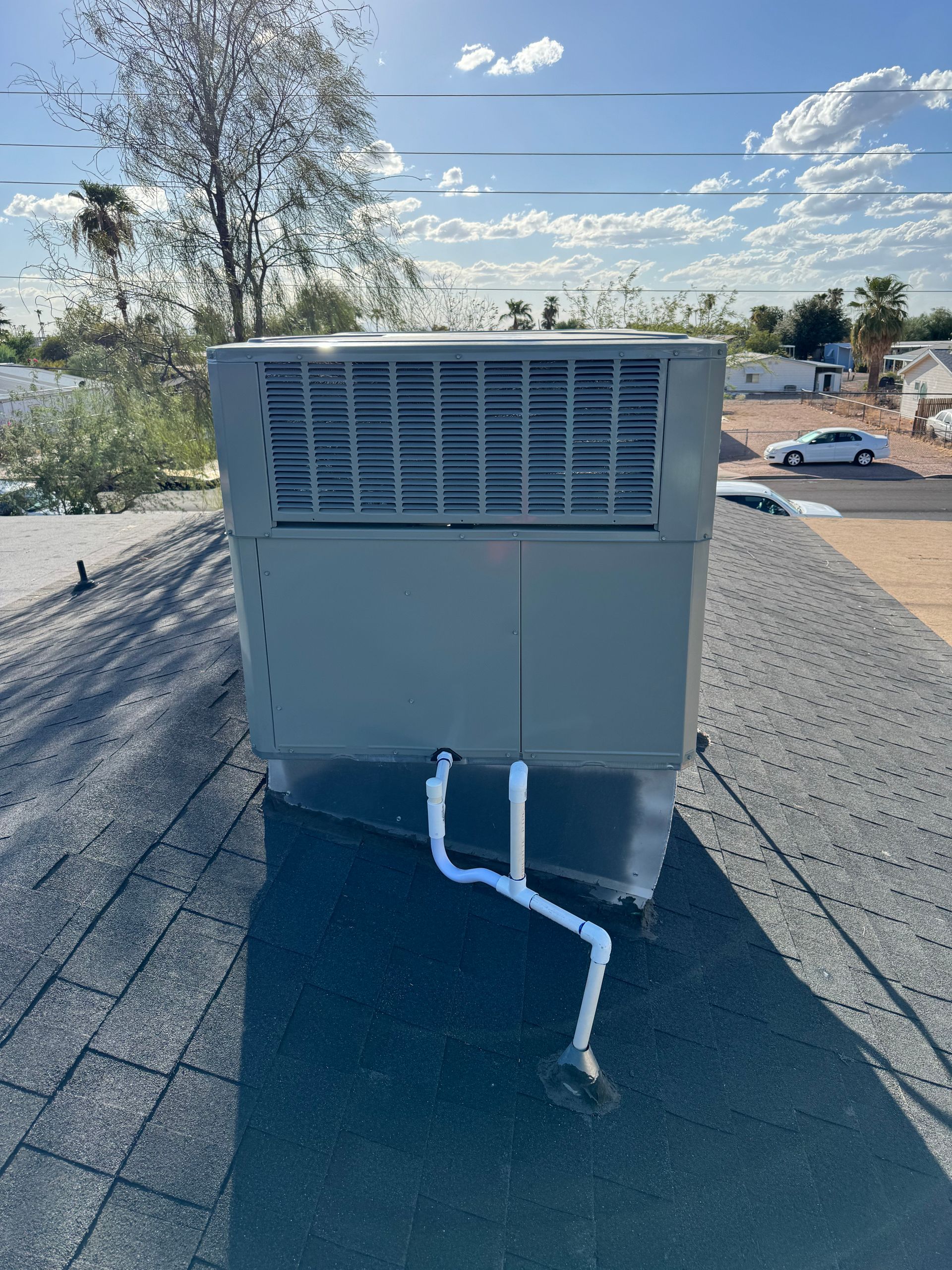 Roof-mounted HVAC unit with white pipes on a gravel rooftop under a sunny blue sky