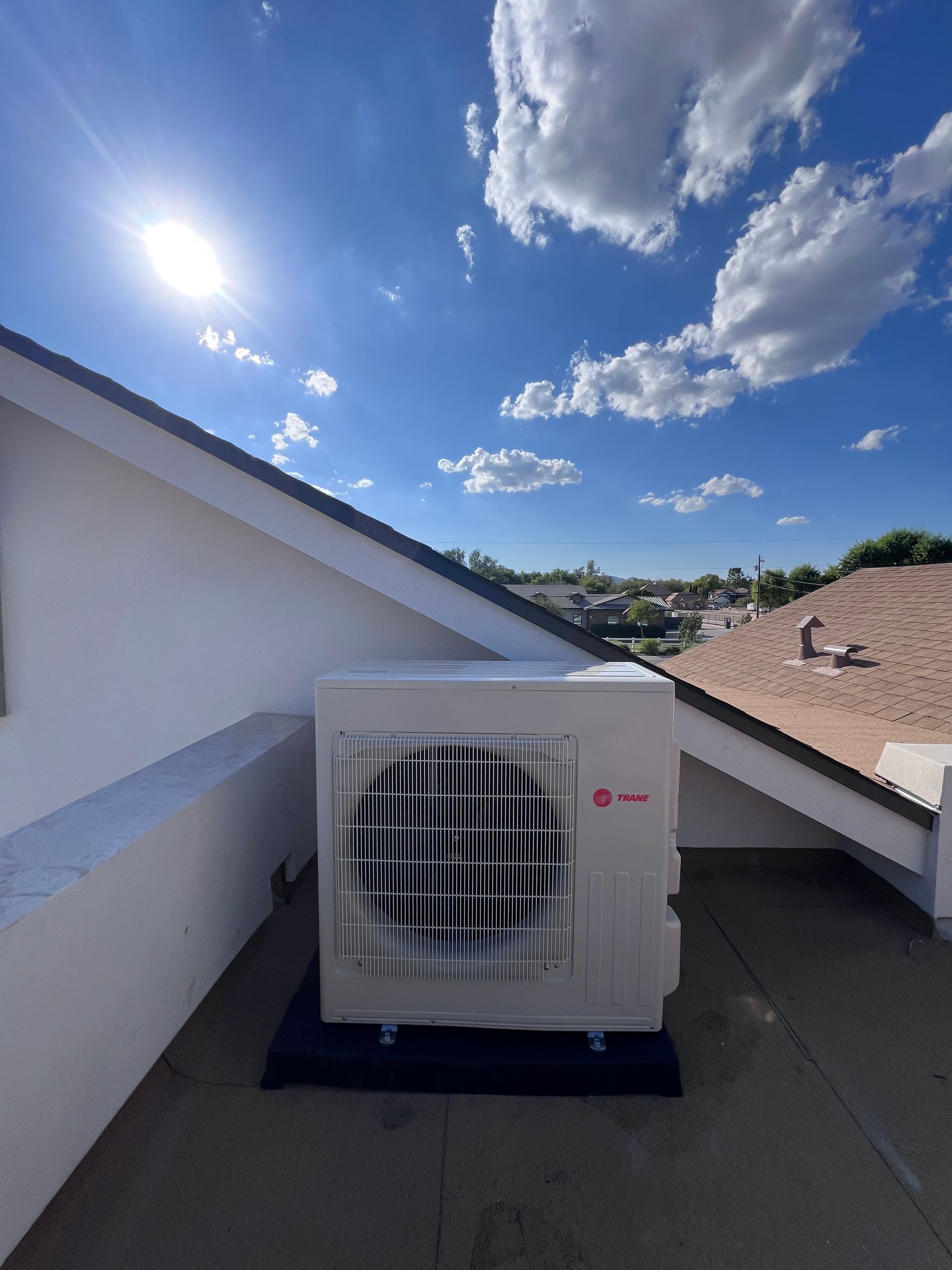 Air conditioner unit on a rooftop under a bright blue sky with clouds