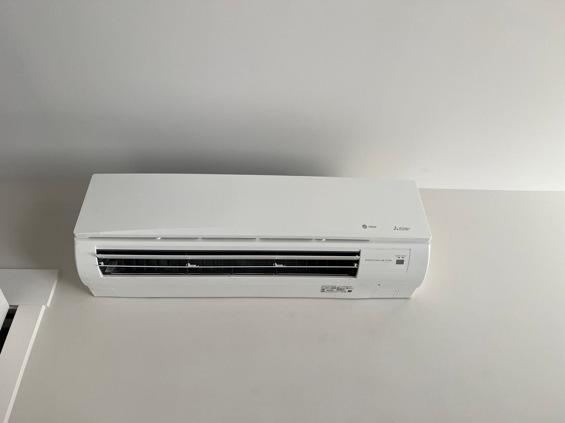 White wall-mounted air conditioner under a ceiling, with a gray shadow above it.
