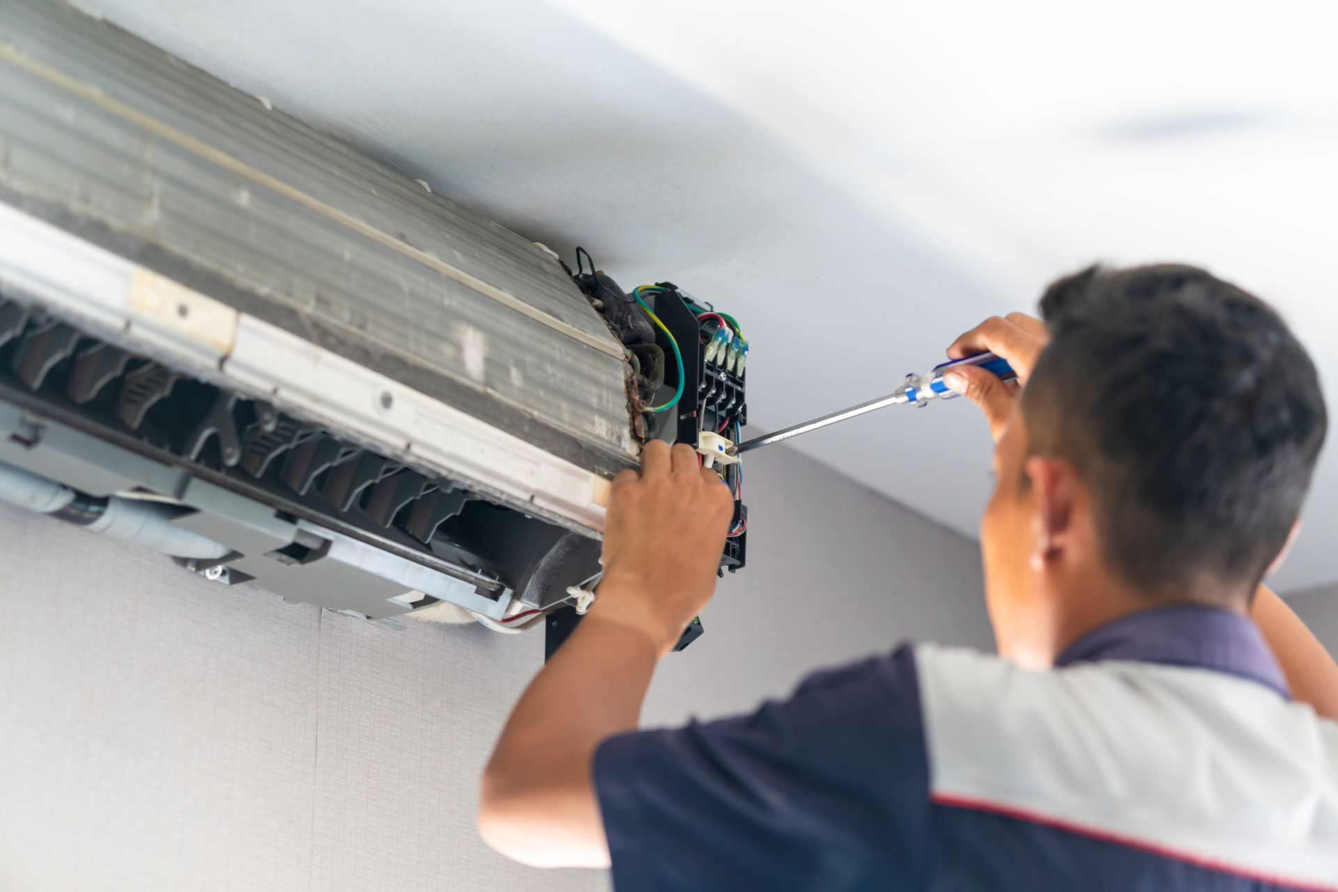 A man is fixing an air conditioner with a screwdriver.
