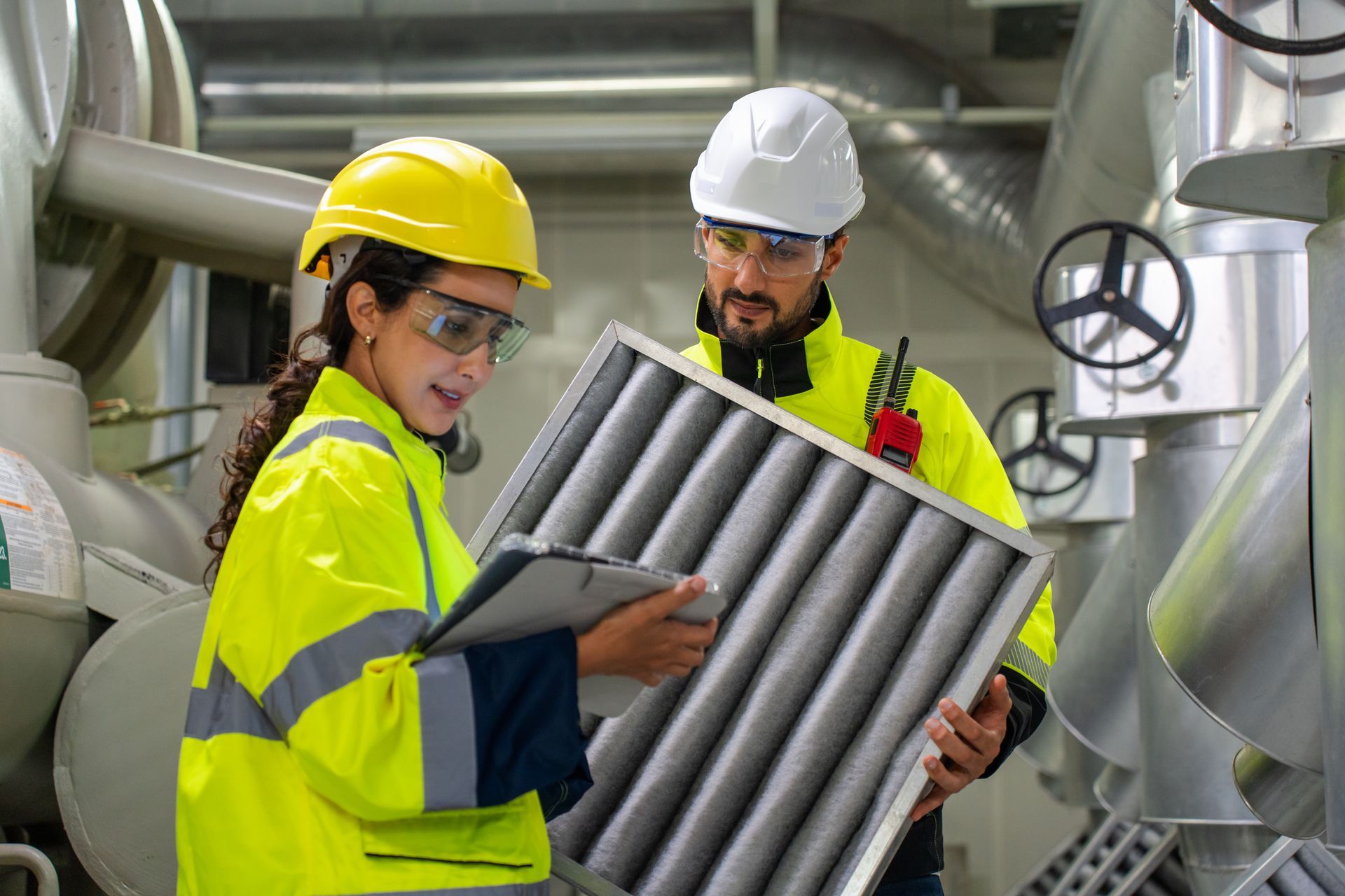 Two engineers in safety gear examining an air filter in an industrial setting.