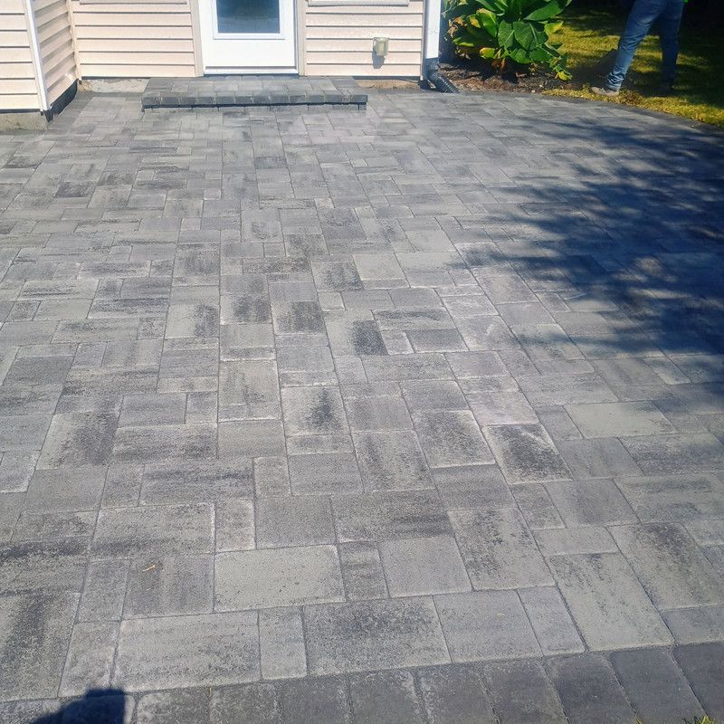 Gray stone paver patio outside a light beige house with a doorway.