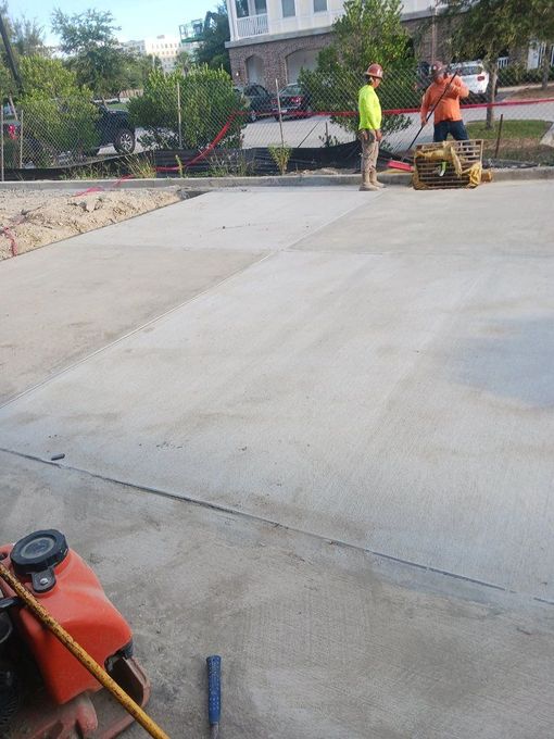 Two construction workers using a plate compactor on a newly poured concrete surface.