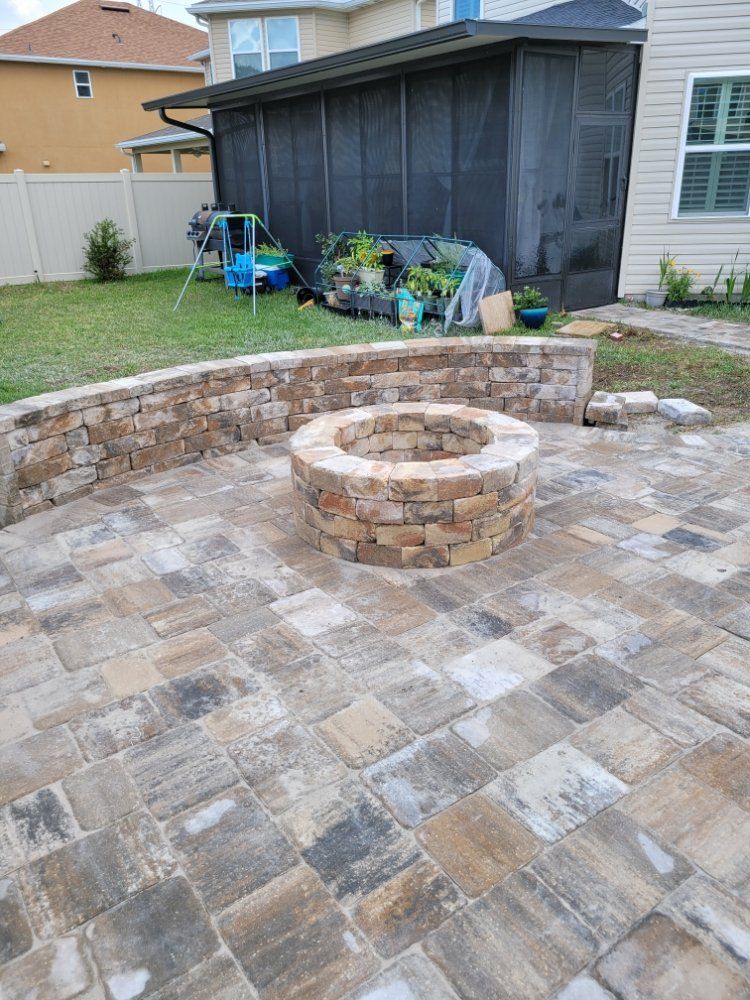 Stone patio with built-in fire pit and retaining wall in a backyard setting.