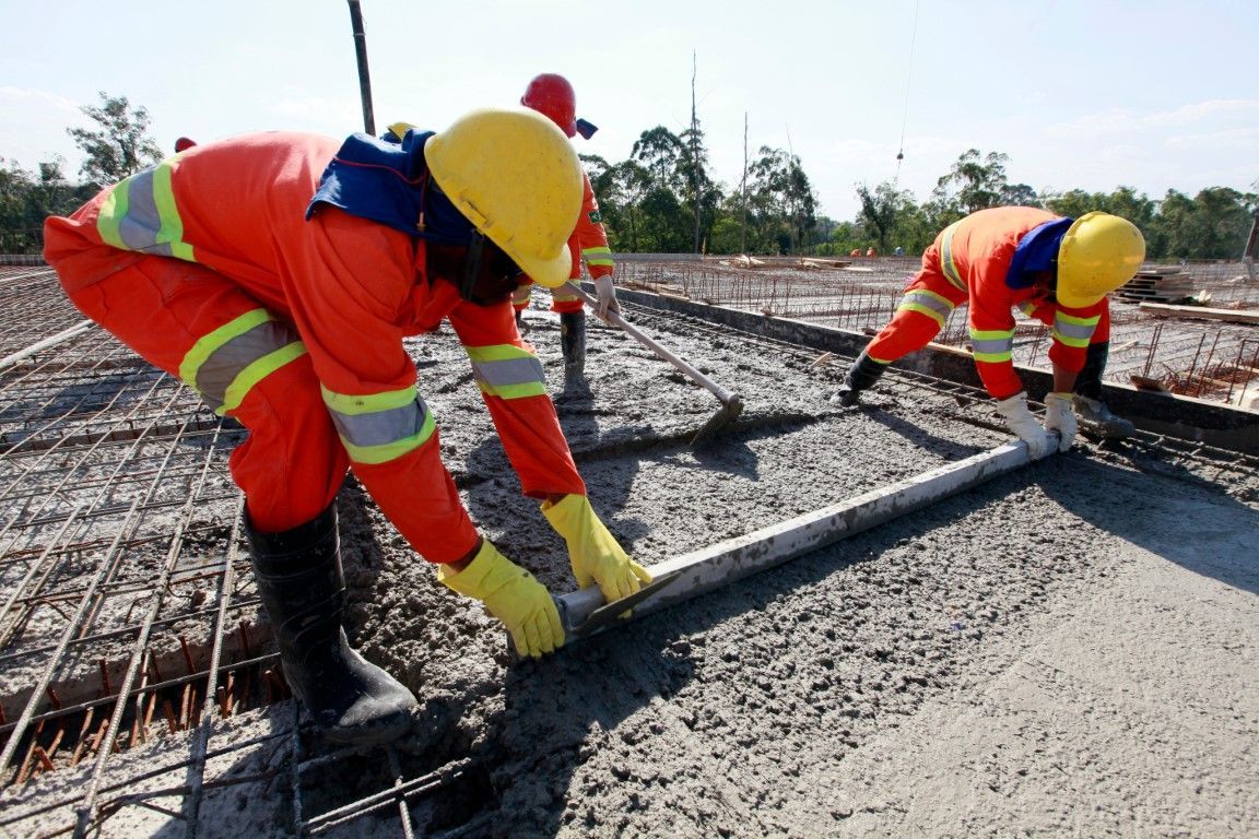 Construction workers leveling wet concrete with long screeds.