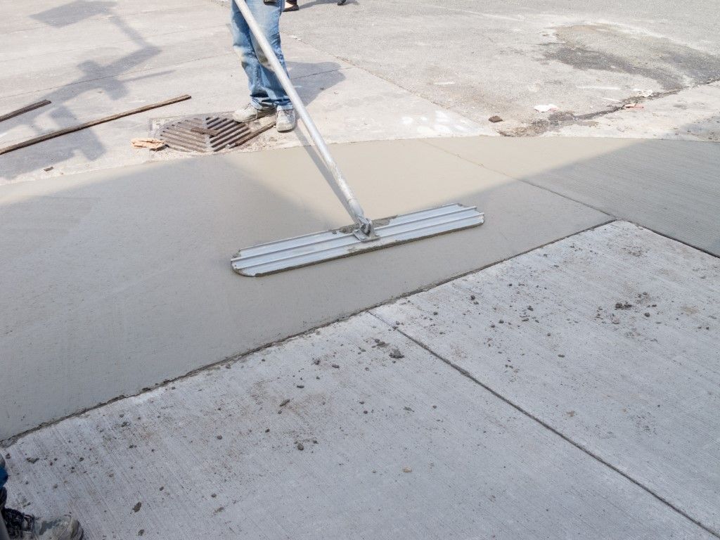 Person smoothing wet concrete with a long-handled tool on a paved surface.