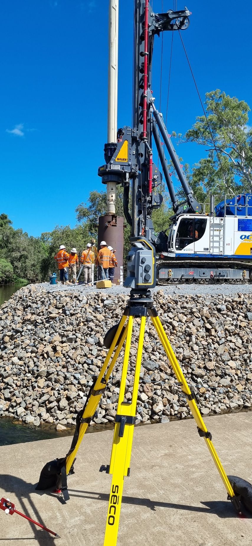 Yellow Tripod in Front of Construction Site With Workers — Next Step Surveying in Coolum, QLD