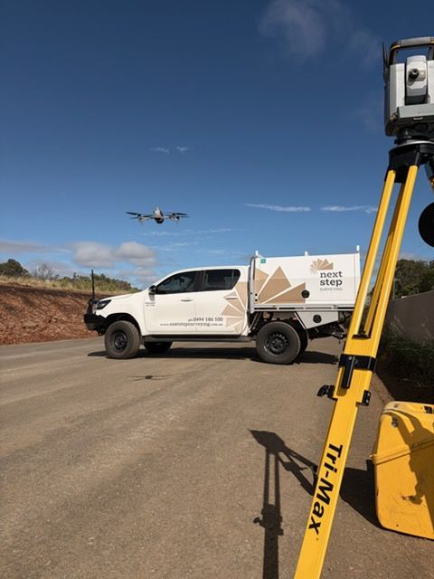 White truck with surveying equipment and drone flying overhead on a clear day— Next Step Surveying in Aroona, QLD
