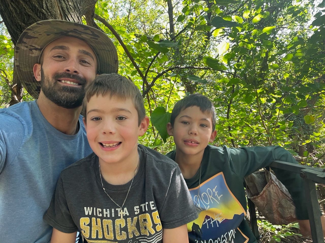 A man and two young boys are posing for a picture in the woods.