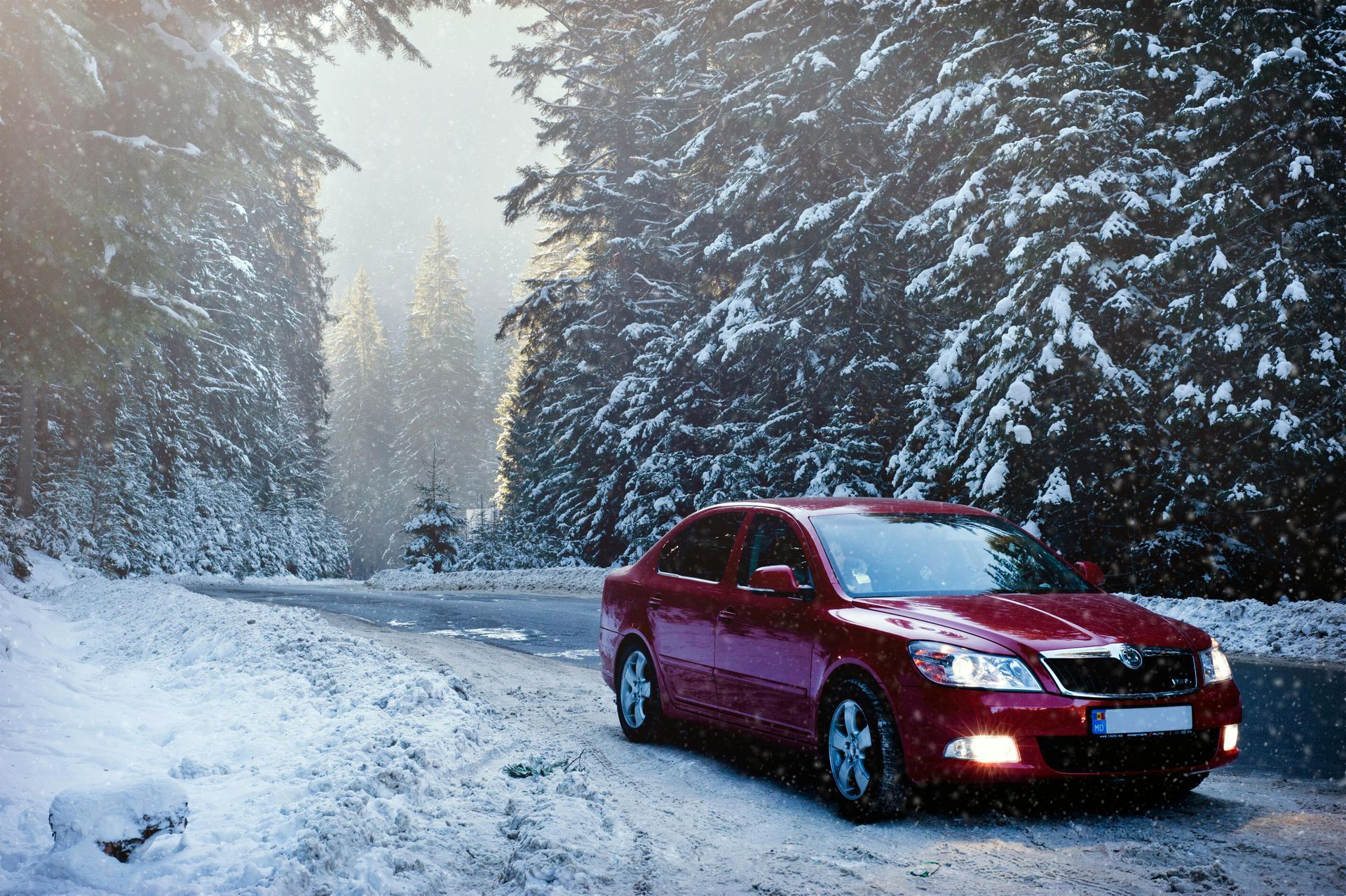 A red car is driving down a snowy road in the woods.
