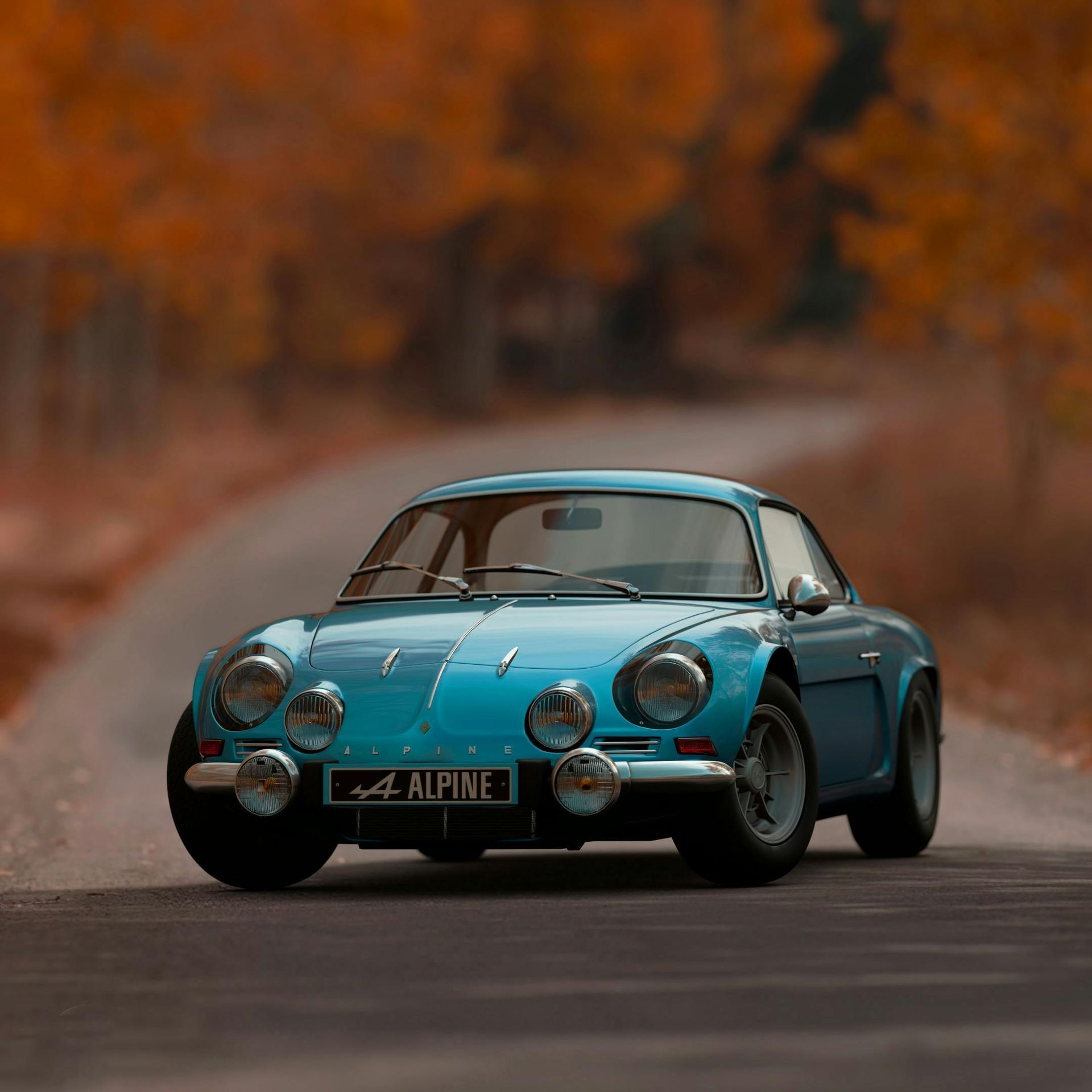 A blue alpine car is driving down a country road.