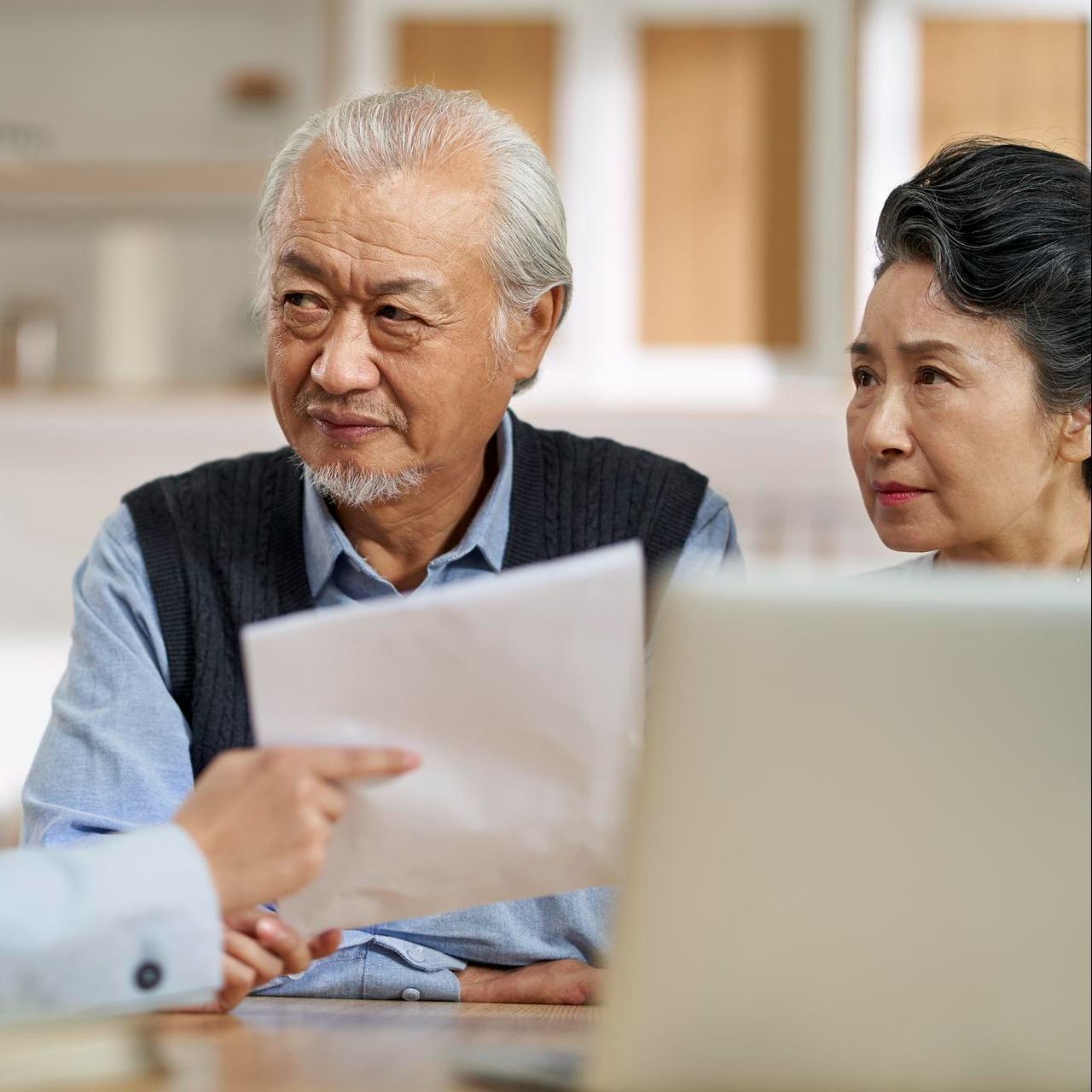 A man and a woman are sitting at a table looking at a laptop.