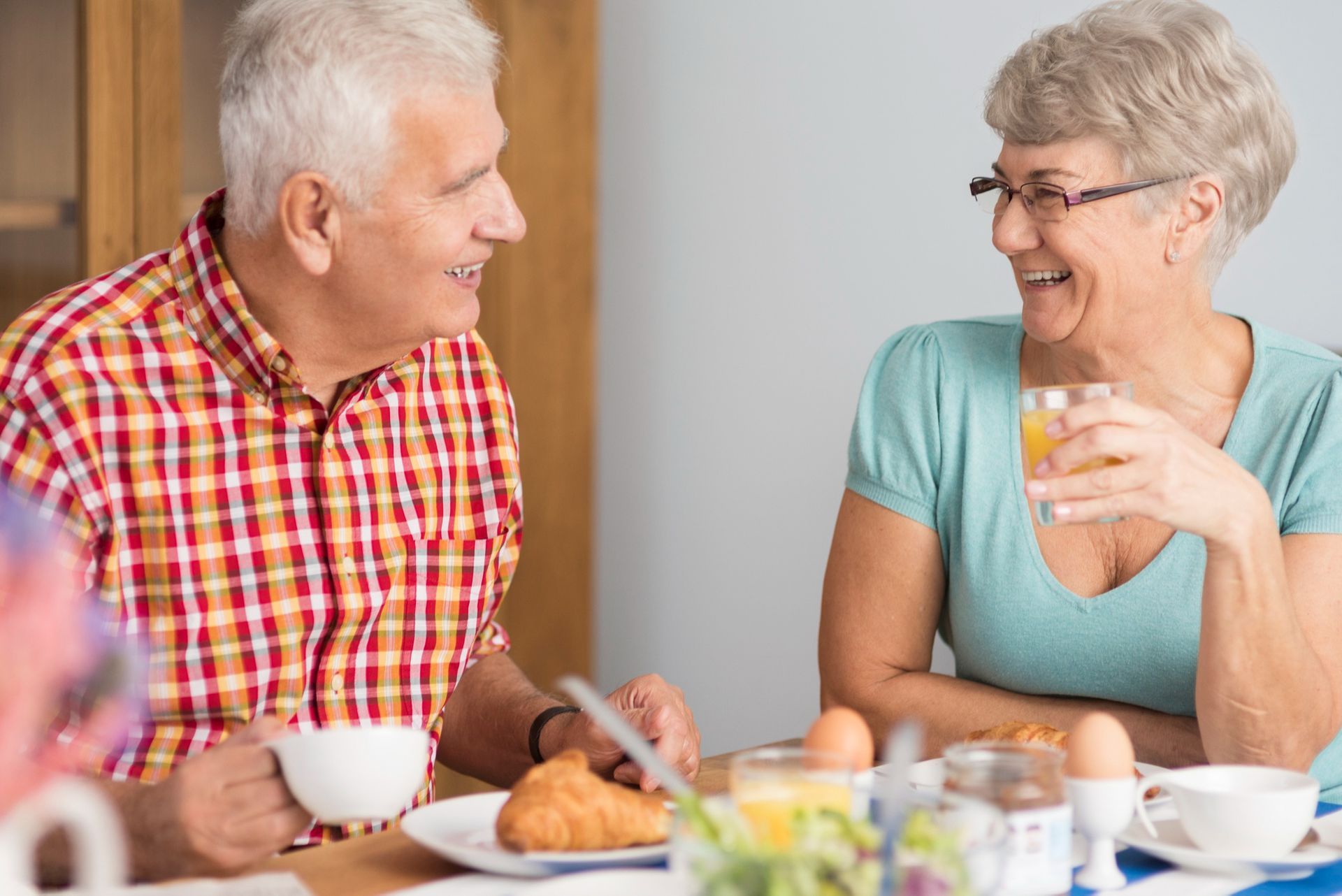 An elderly couple is sitting at a table eating breakfast and drinking orange juice.