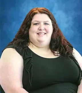 A woman with long red hair is wearing a black tank top and smiling.