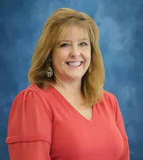 A woman in a red shirt and earrings is smiling for the camera.