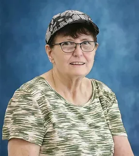A woman wearing glasses and a hat is sitting in front of a blue background.