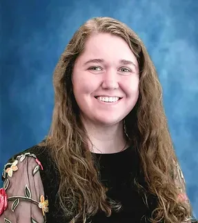 A young woman with long hair is smiling in front of a blue background.