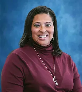 A woman wearing a maroon turtleneck and a necklace is smiling for the camera.