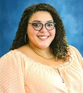 A woman wearing glasses and a polka dot shirt is smiling for the camera.
