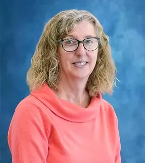 A woman wearing glasses and a red sweater is standing in front of a blue background.