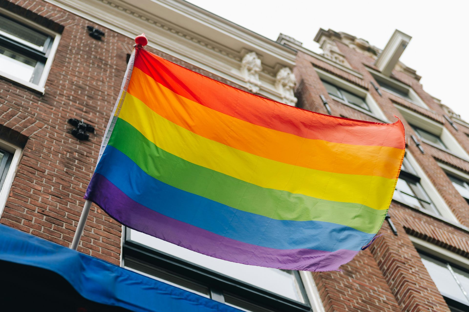 A rainbow flag is flying in front of a brick building.