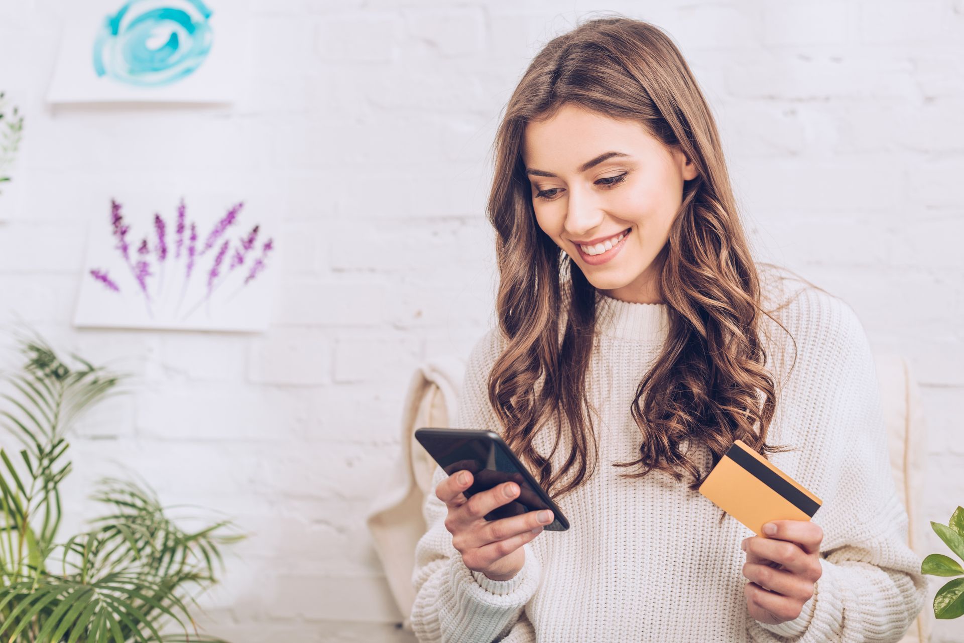 Smiling woman holding a credit card and a cell phone signing up for online membership and the benefits of special offers