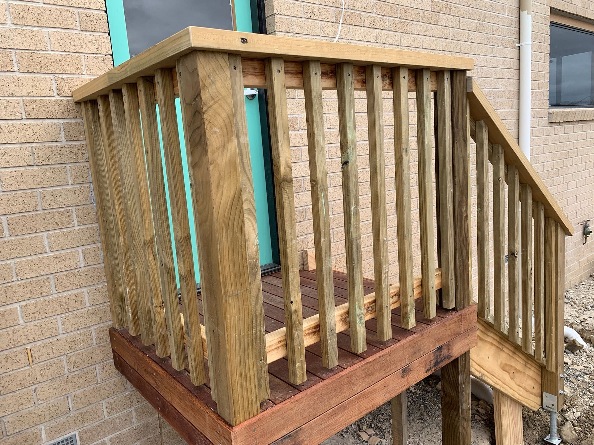 A wooden deck landing and stairs with railings attached to the brick exterior of a building with a light blue door.
