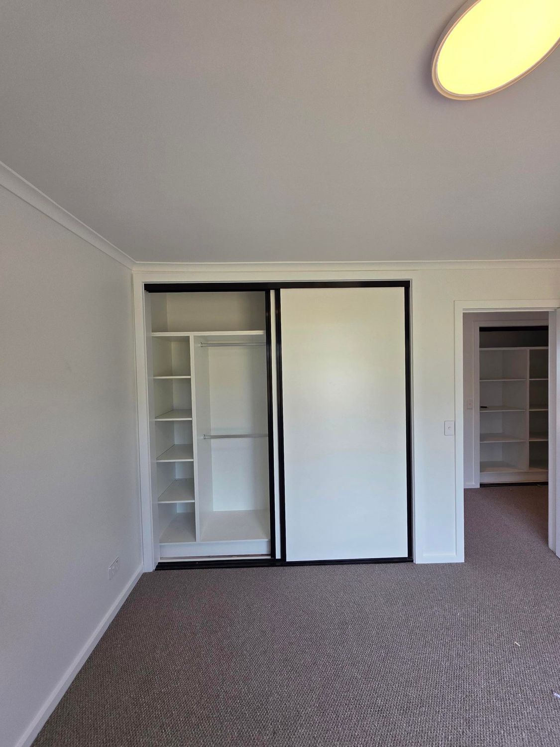 A carpeted room with a white sliding-door closet and shelving, plus a view into an adjacent room with a similar closet.