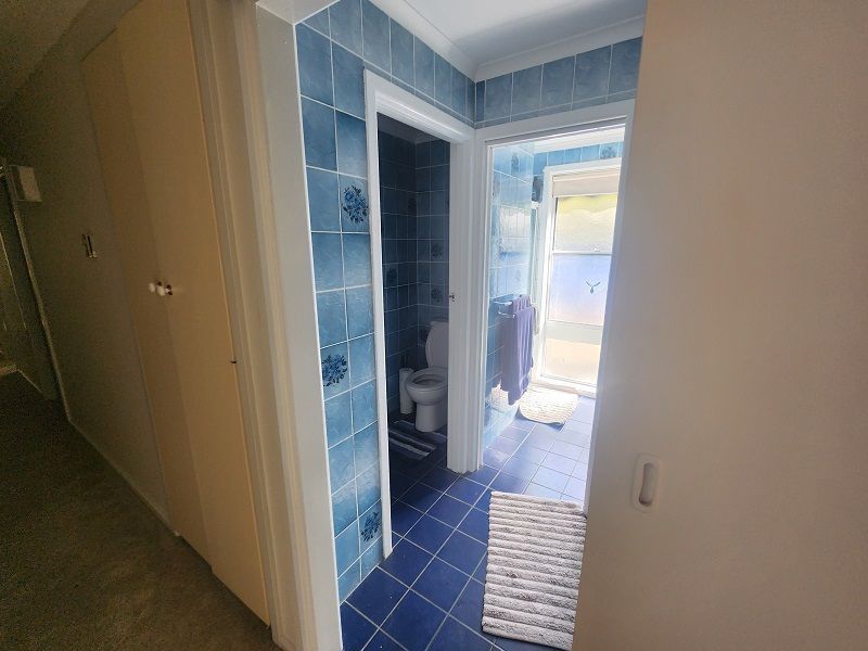 A hallway leading to a bathroom with blue tiles and a toilet.