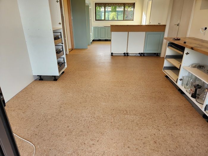 A kitchen with a cork floor and white cabinets.