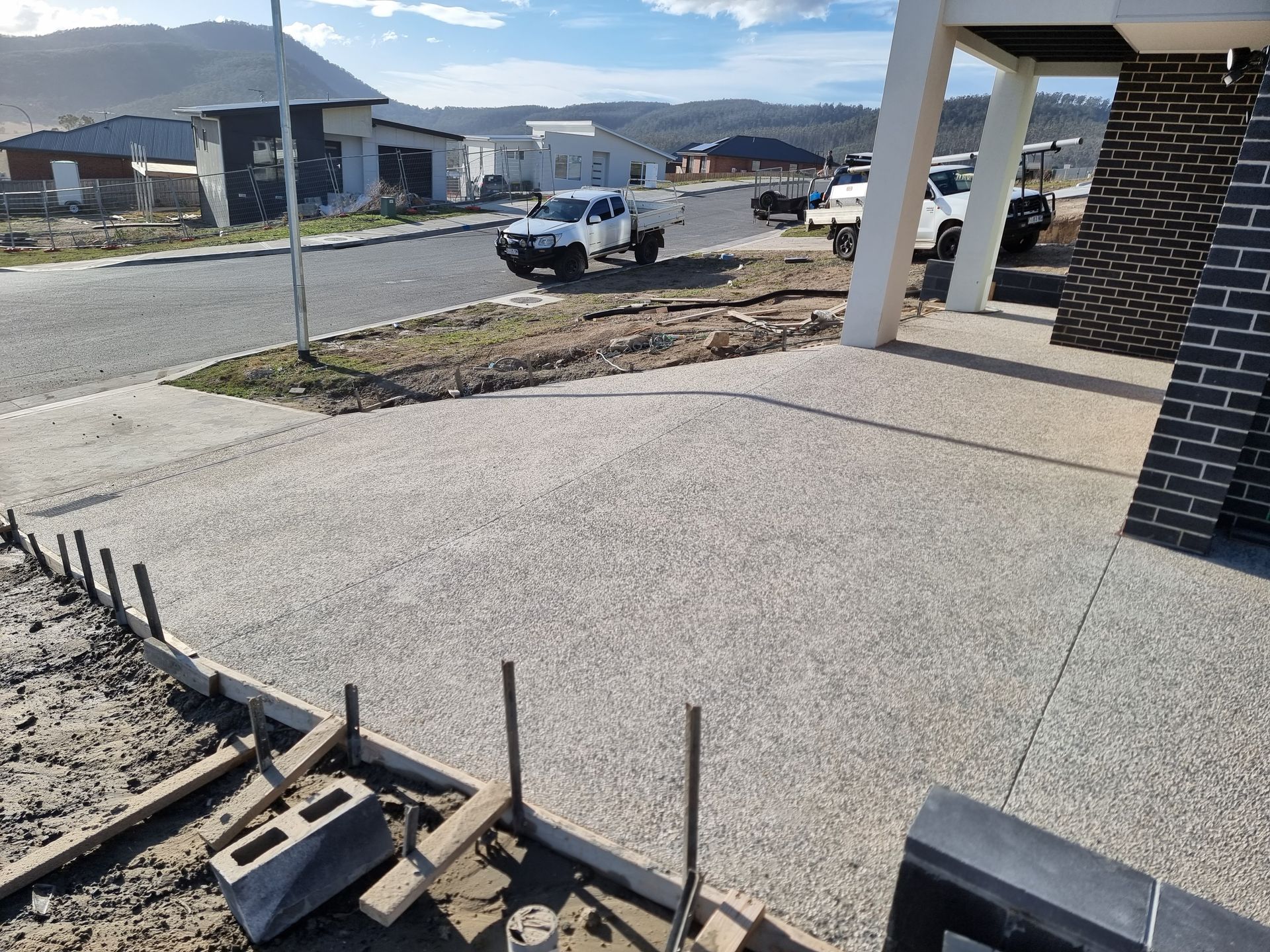 New exposed aggregate concrete driveway surface under construction, showing framing and a neighborhood setting.