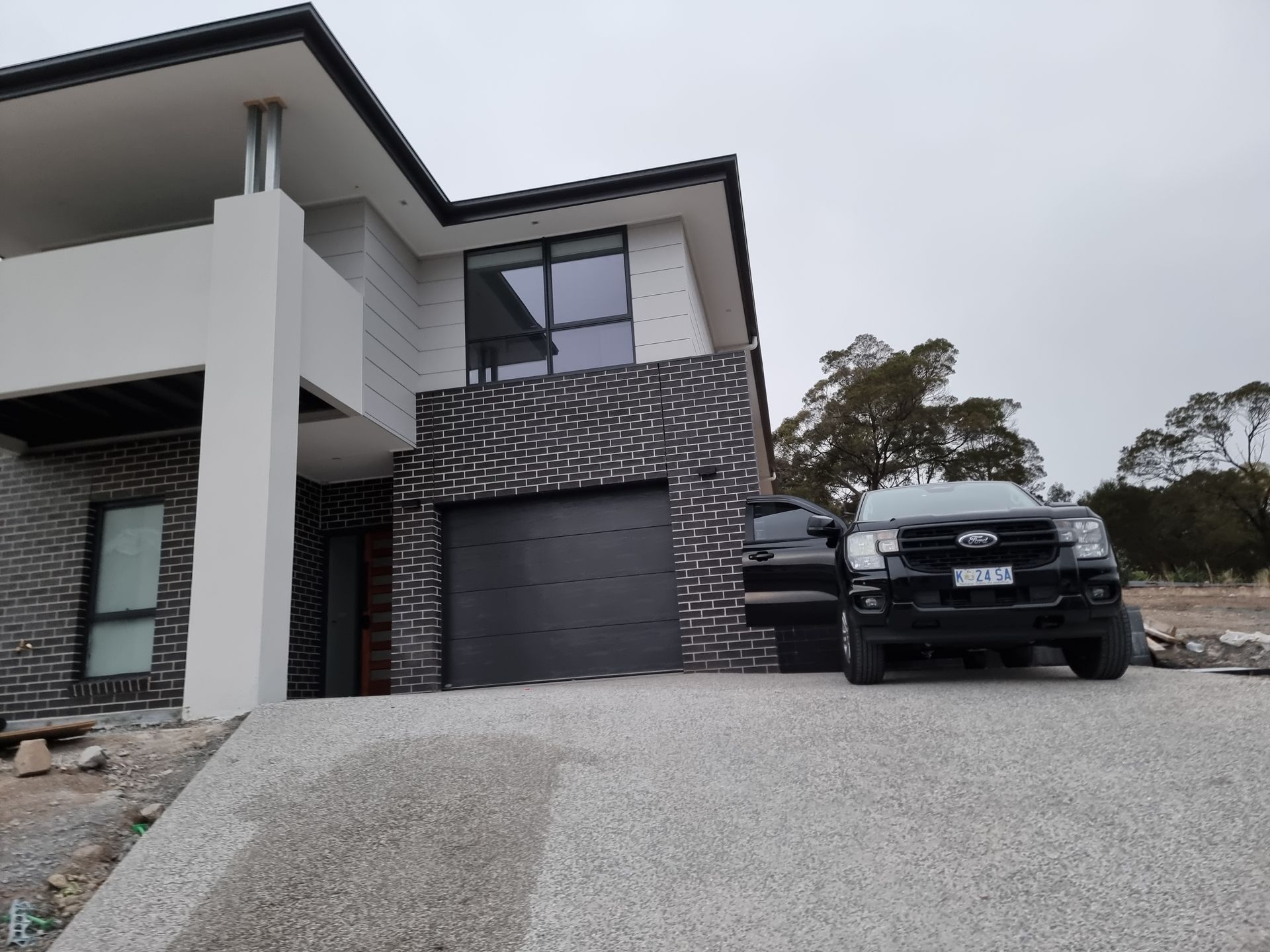 A two-story modern house with a dark brick facade and white accents, featuring a garage with a black pickup truck parked.
