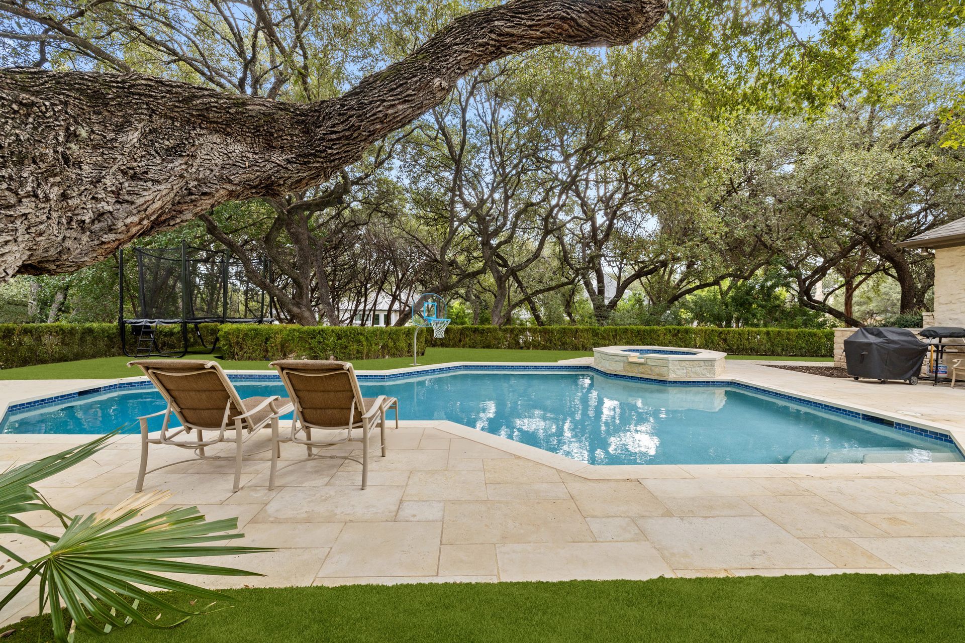 A large swimming pool surrounded by trees and lawn chairs in a backyard.