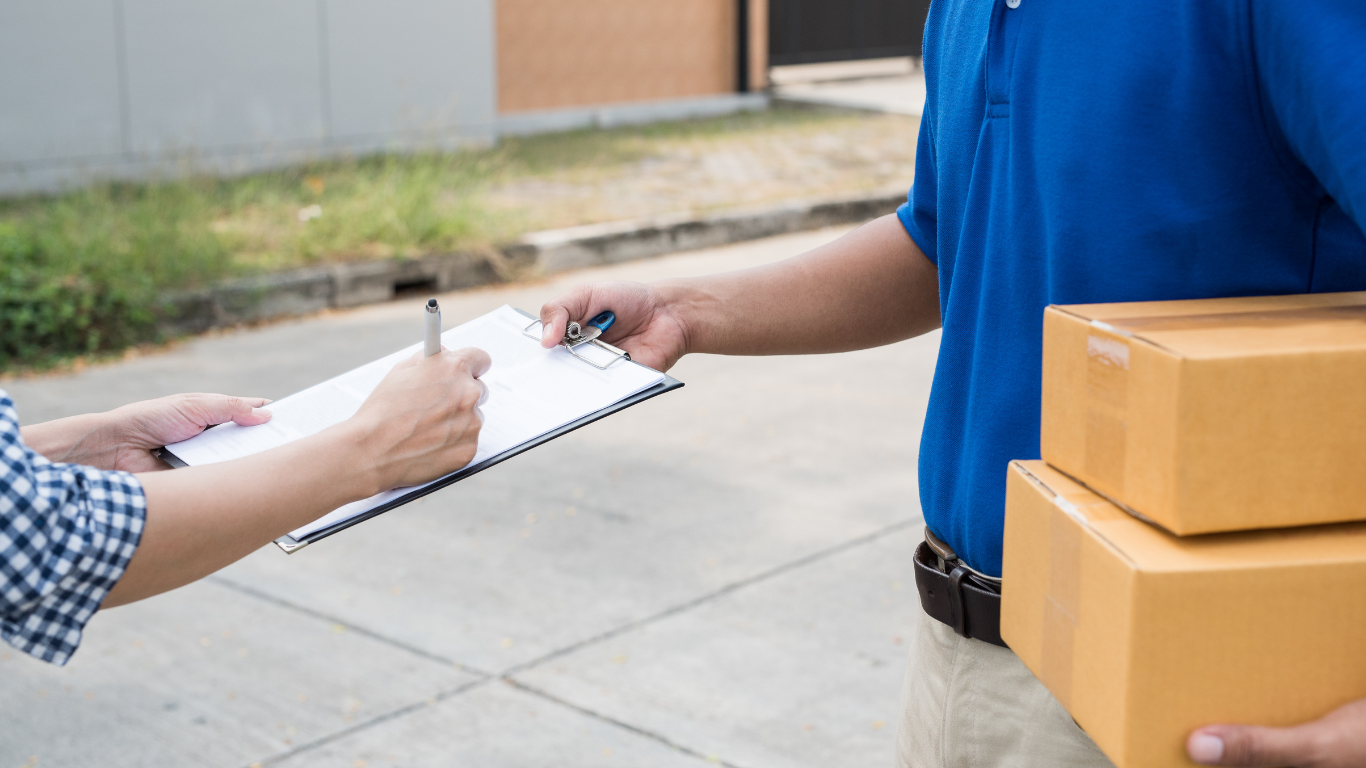Person signing a clipboard from a delivery person holding two brown packages.