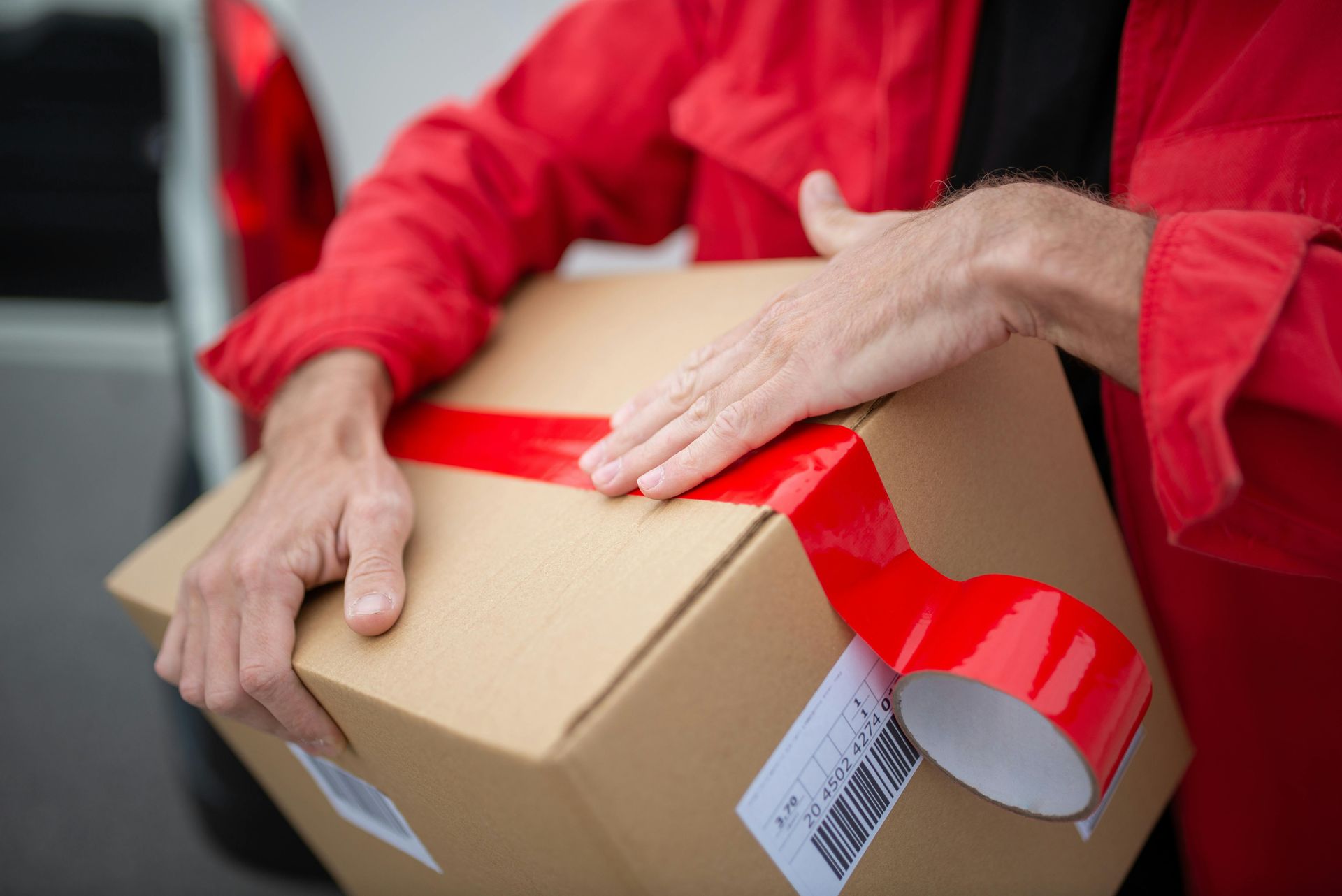 Person in red shirt holding a cardboard box sealed with red tape
