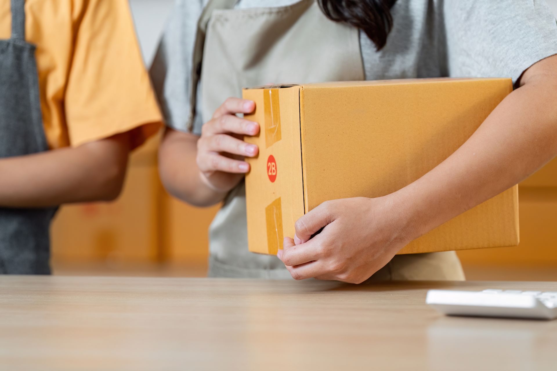 Two people holding a brown cardboard box, likely for shipping, indoors.
