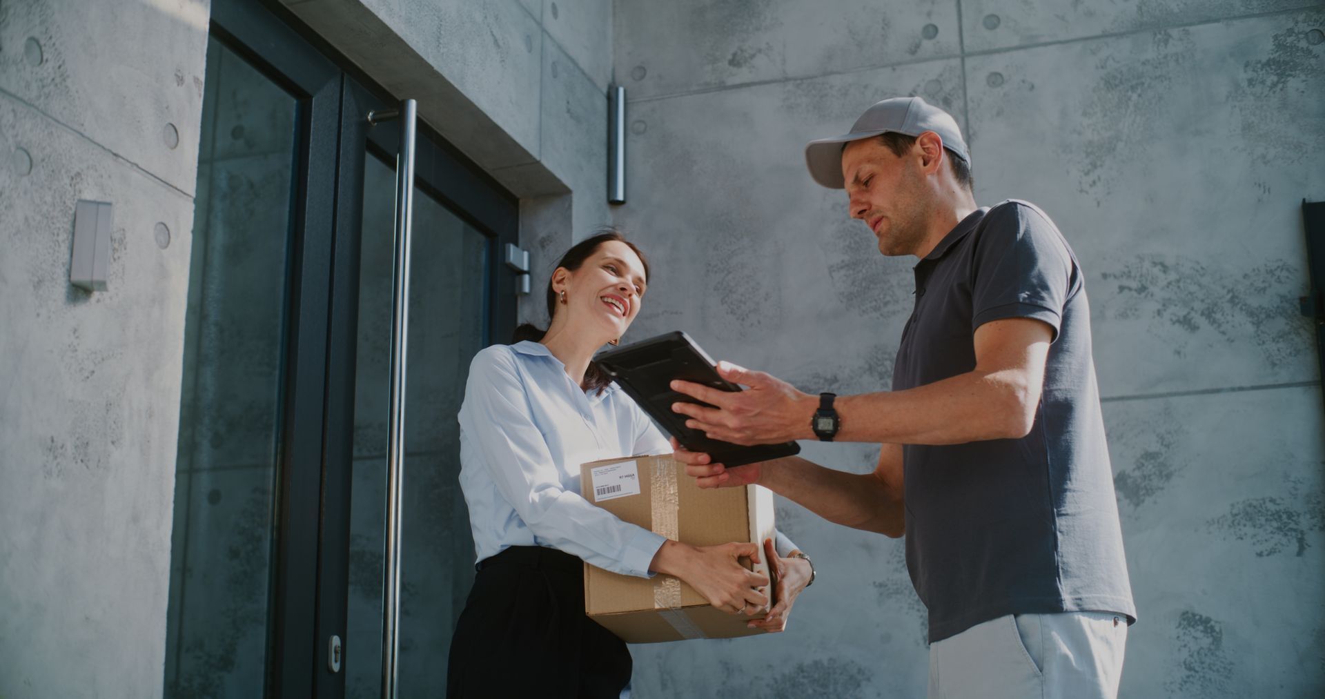 Delivery person handing a package to a woman at a doorway; the woman smiles and holds the box.