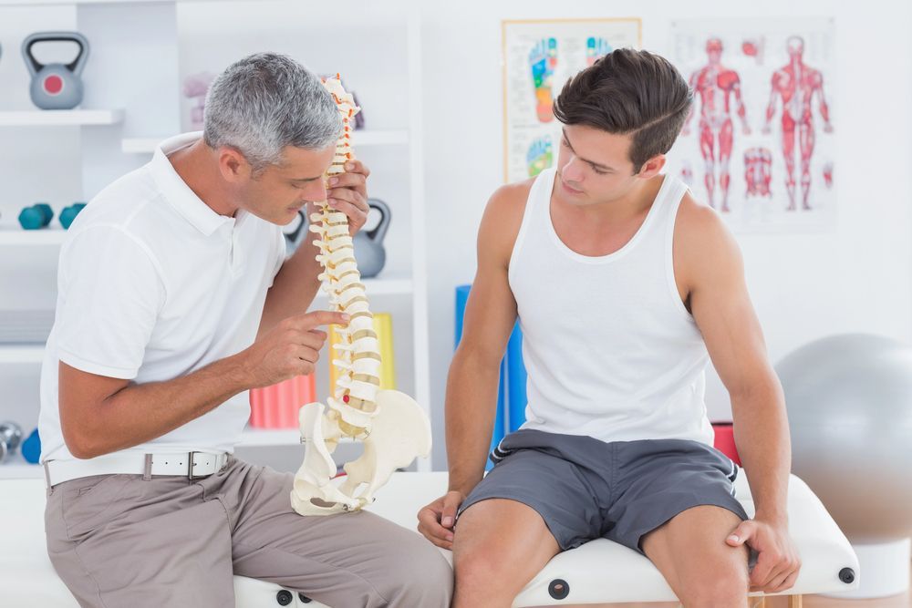 A man is holding a model of a spine while another man looks at it.