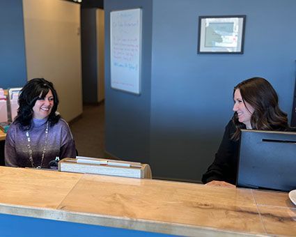 Two women are sitting at a counter in an office talking to each other.
