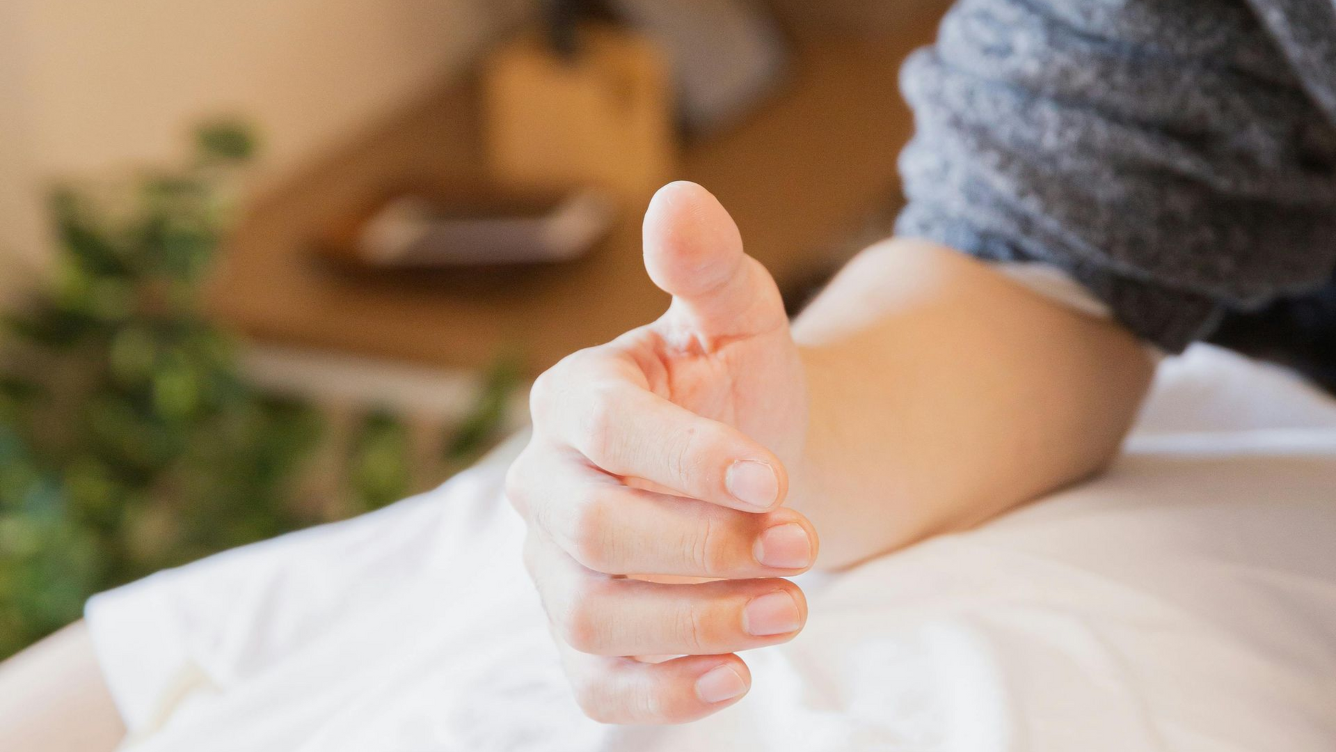Hand reaching out, offering a thumbs up gesture, in an indoor setting.