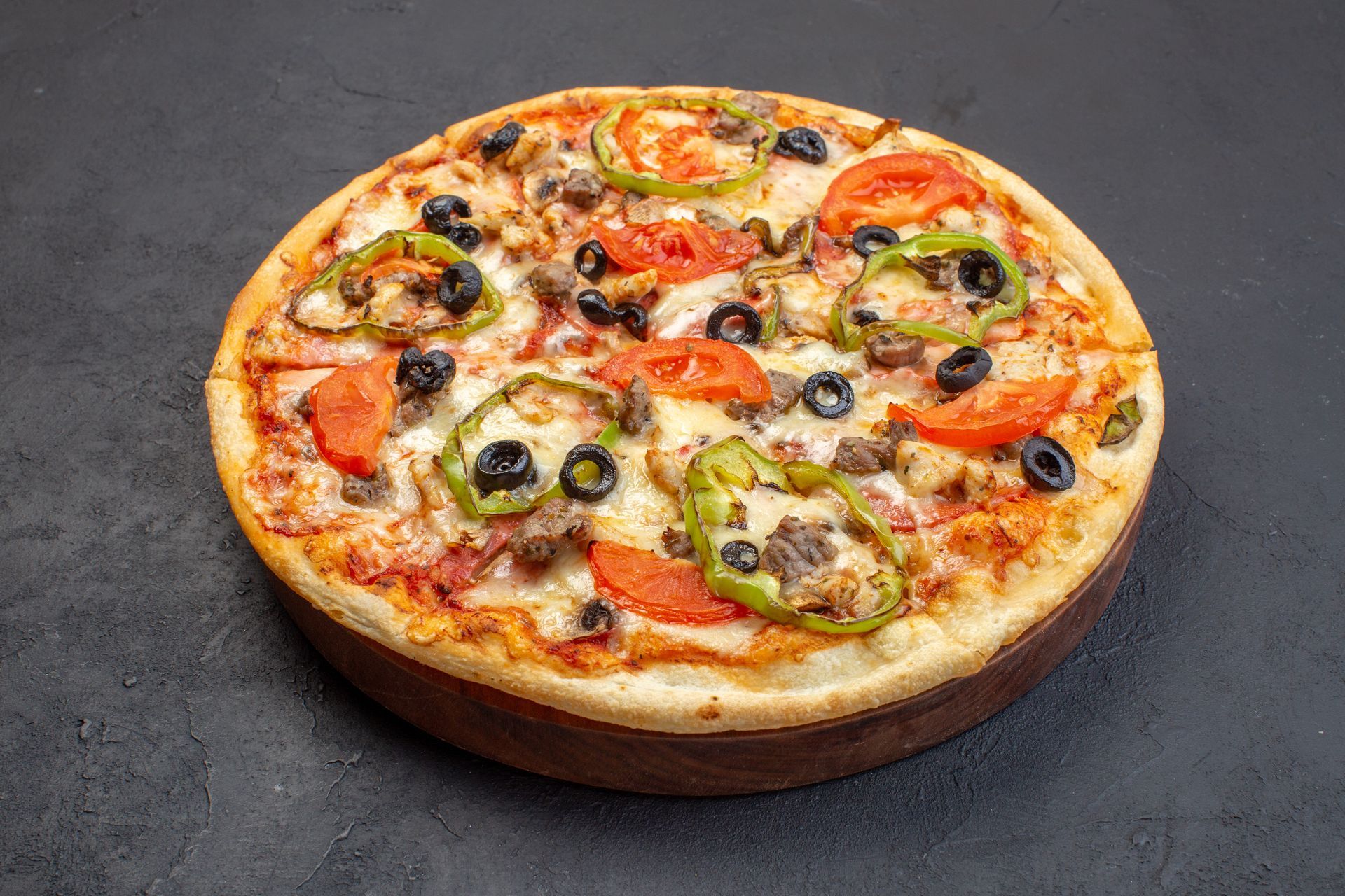 A pizza with tomatoes , peppers , olives and cheese on a wooden cutting board.
