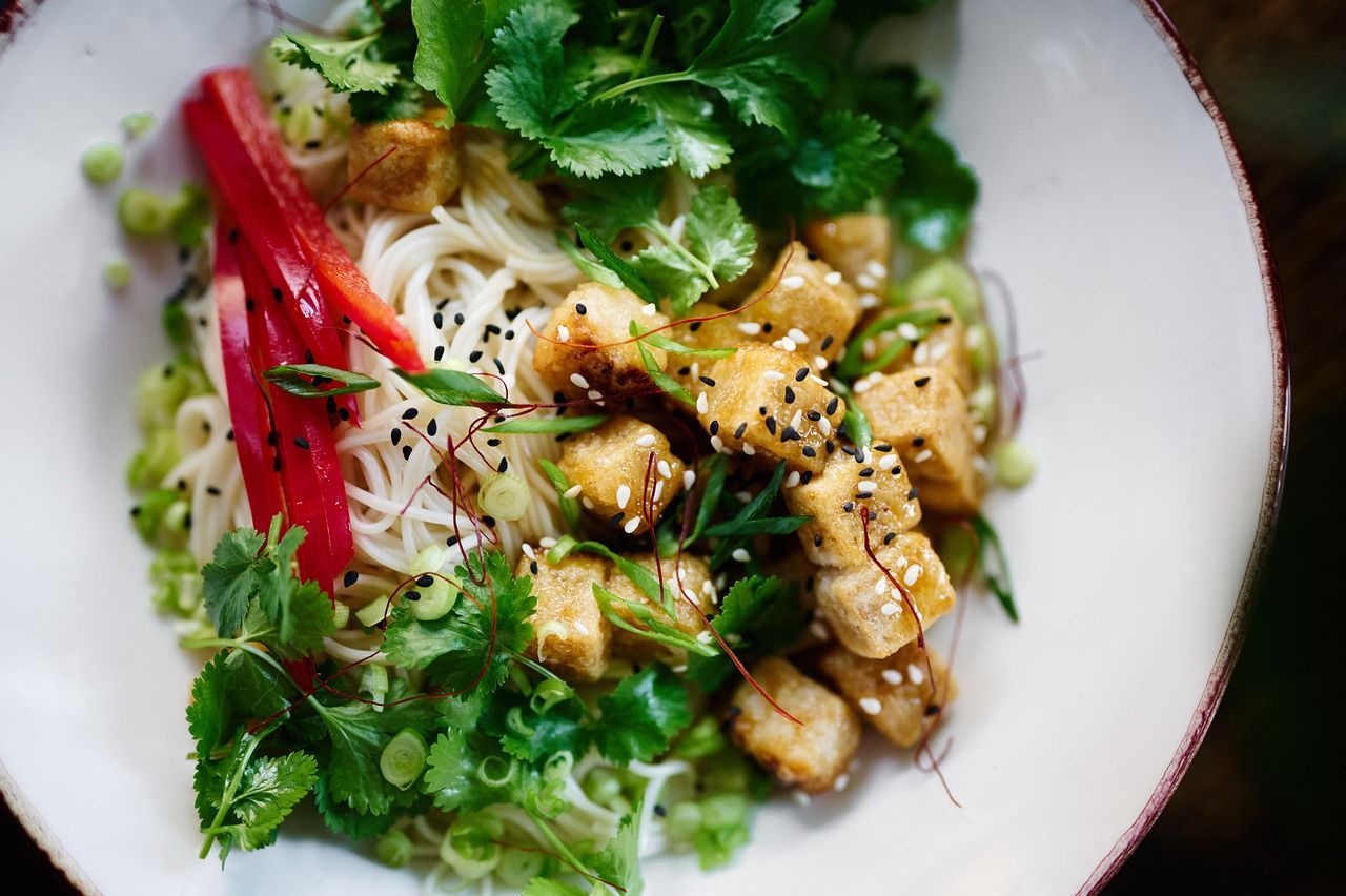 A close up of a plate of food with noodles and vegetables on a table.