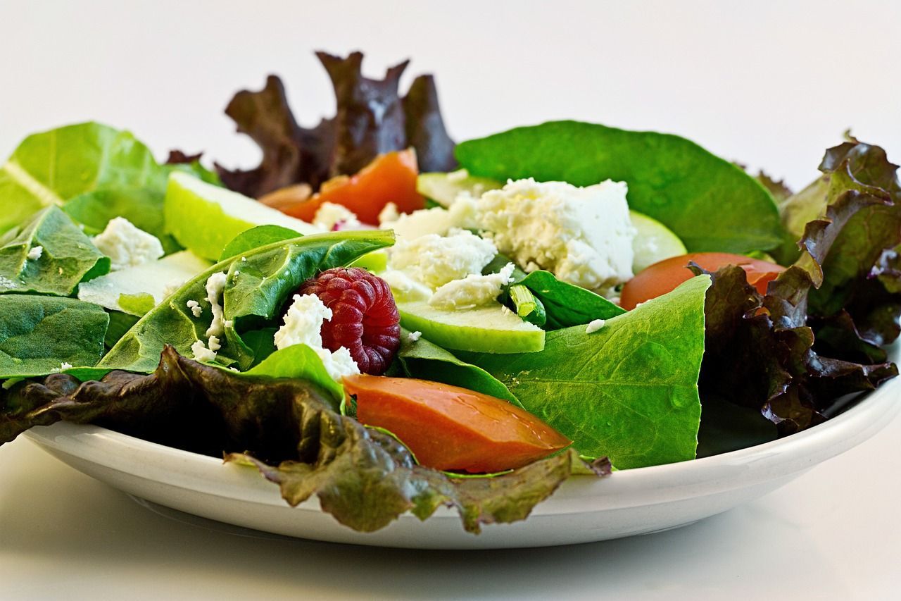 A white plate topped with a salad of lettuce tomatoes and raspberries.