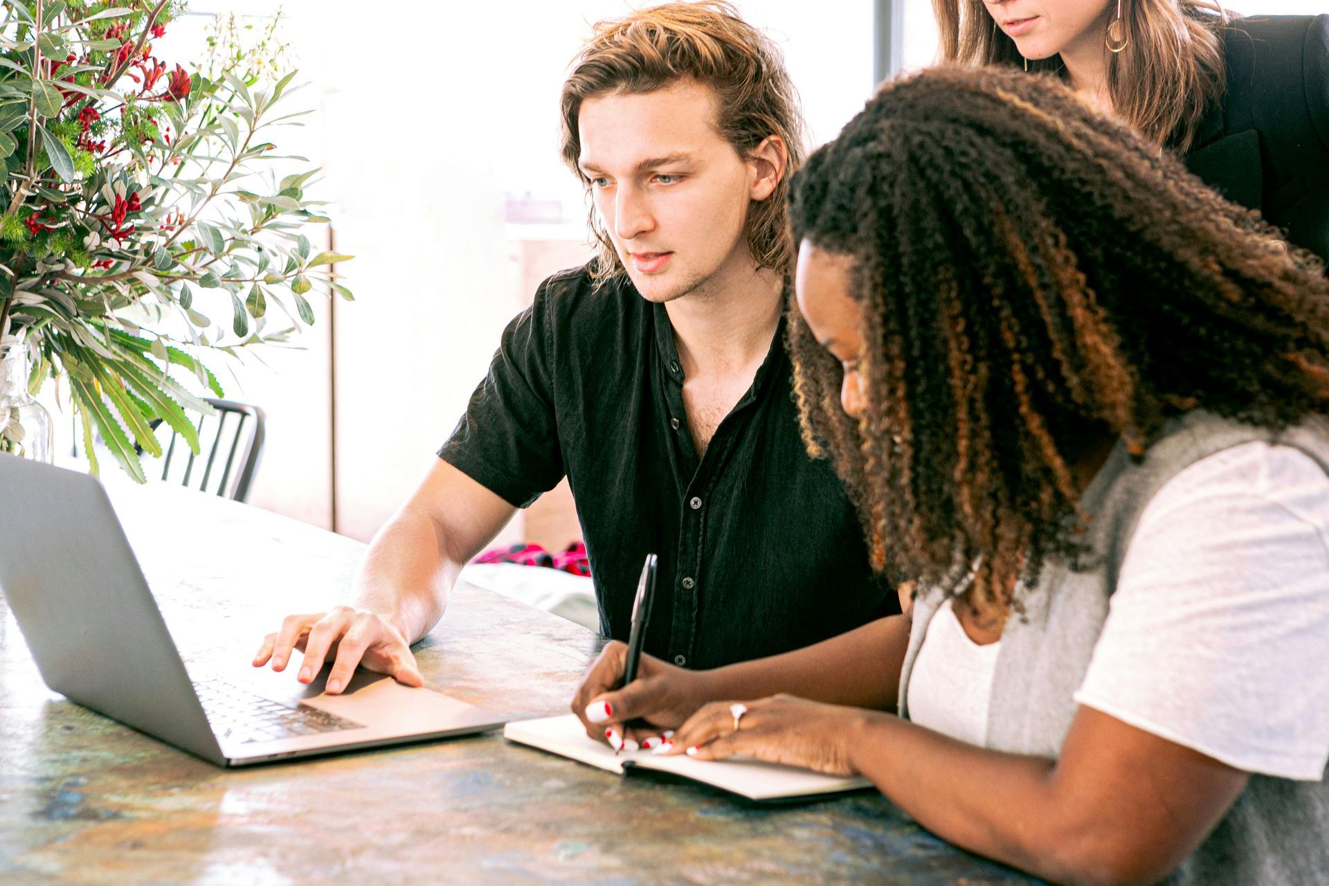 A group of people are sitting at a table looking at a laptop computer.