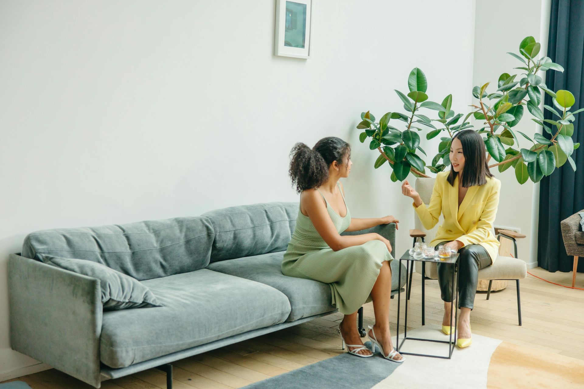Two women are sitting on a couch talking to each other in a living room.