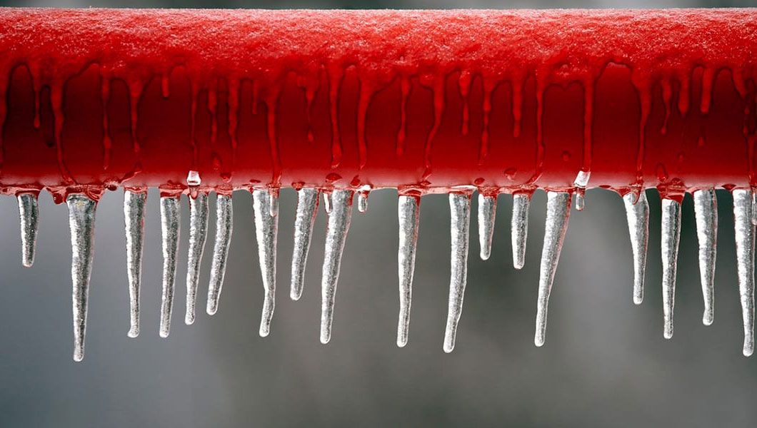 Icicles are hanging from a red pipe.